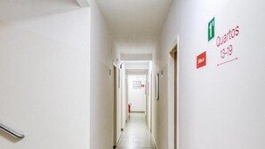 A clean, well-lit hallway with a tiled floor, a handrail on the left, and a sign indicating 'Quartos 13-19' on the right. - Hotel Paulistano (São Paulo)