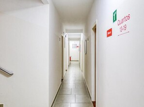 A clean, well-lit hallway with a tiled floor, a handrail on the left, and a sign indicating 'Quartos 13-19' on the right. - Hotel Paulistano (São Paulo)