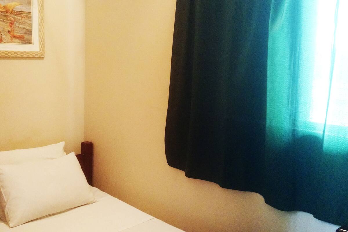 Ein Einzelbett mit weißer Bettwäsche in einem Zimmer mit schlichter Wand und einem gerahmten Bild.
