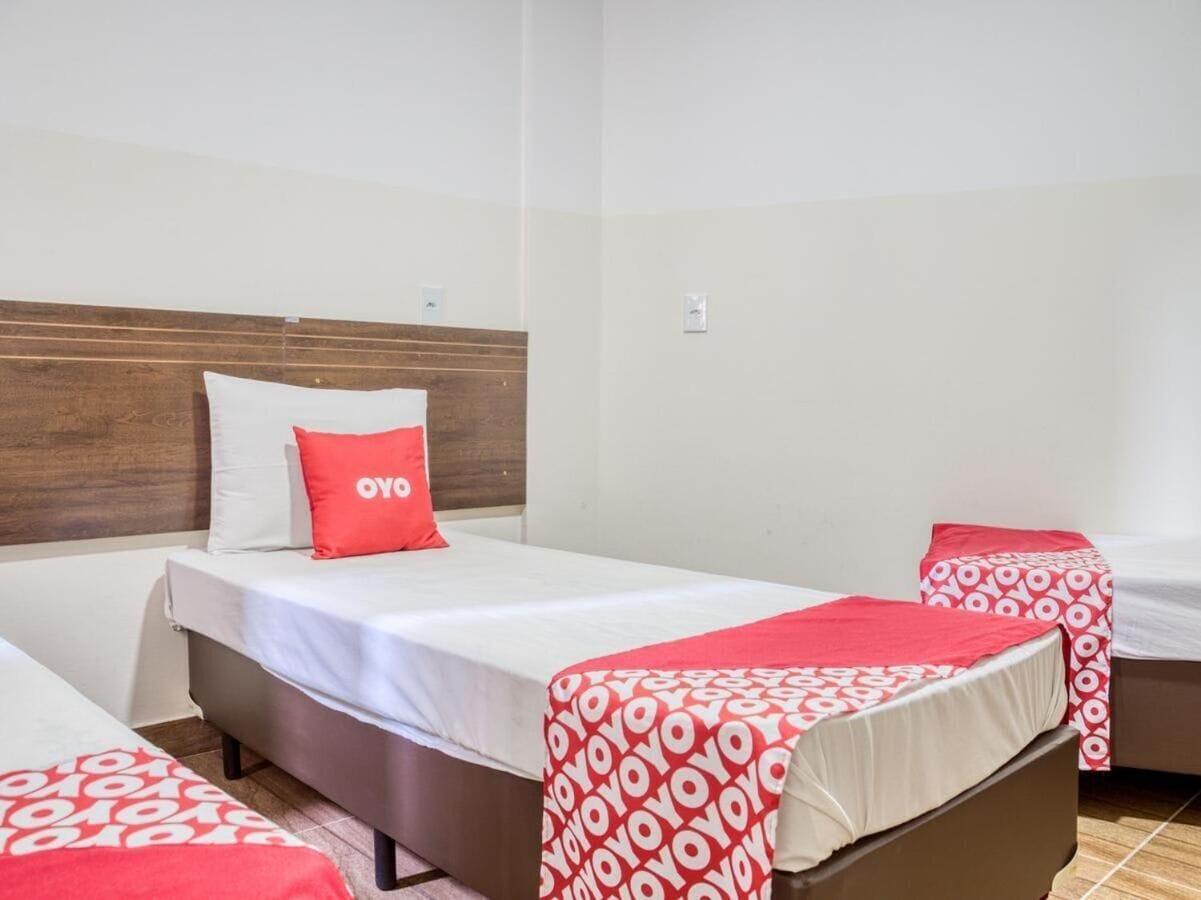 Quarto de hotel com duas camas, cada uma com uma colcha de padrão vermelho e branco e um travesseiro com a palavra "YOYO".