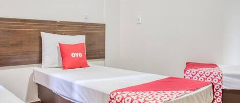 Quarto de hotel com duas camas, cada uma com uma colcha de padrão vermelho e branco e um travesseiro com a palavra "YOYO".