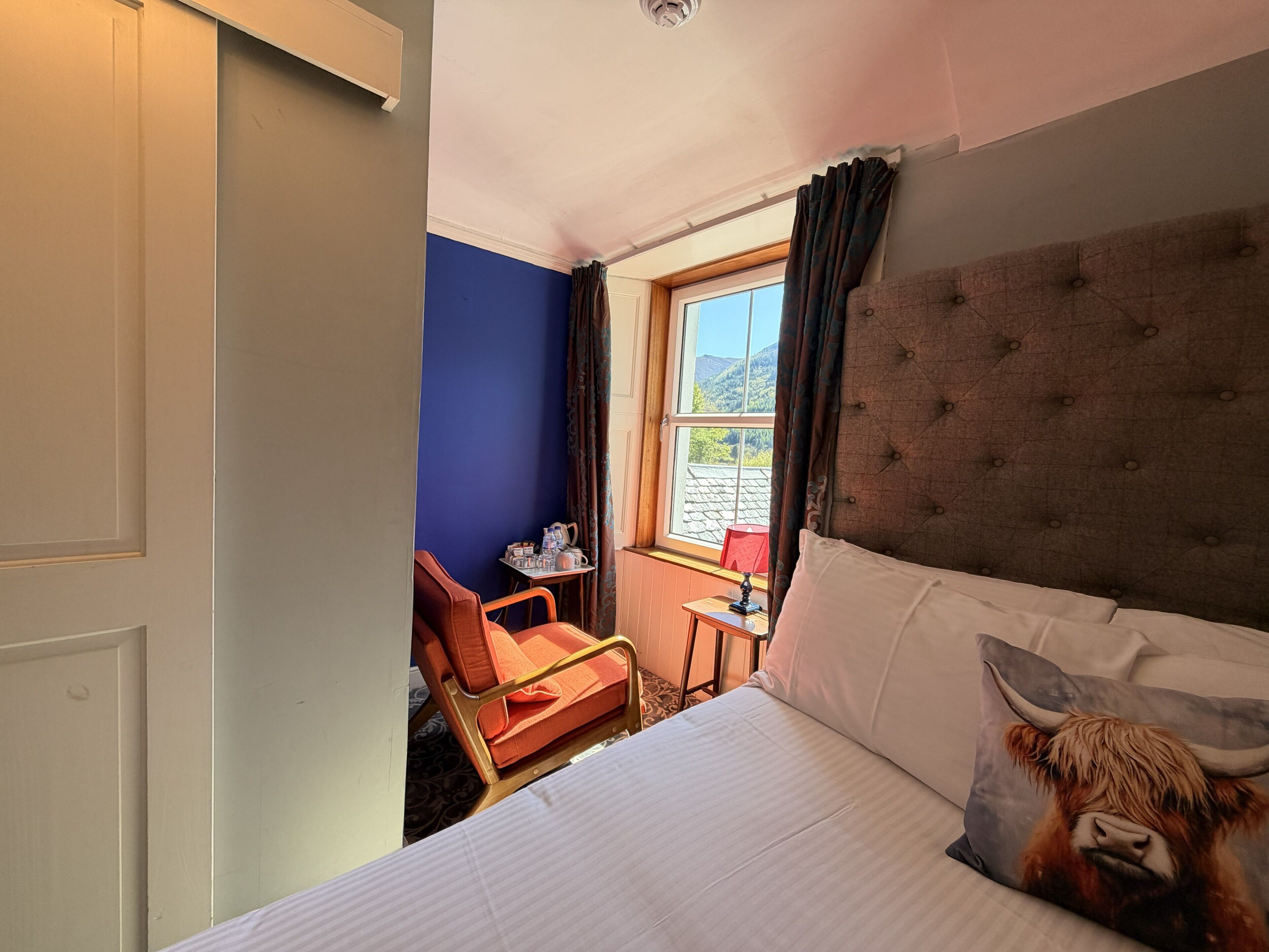 A hotel room with a bed, a chair, a small table, and a window with curtains.