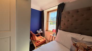 A hotel room with a bed, a chair, a small table, and a window with curtains.