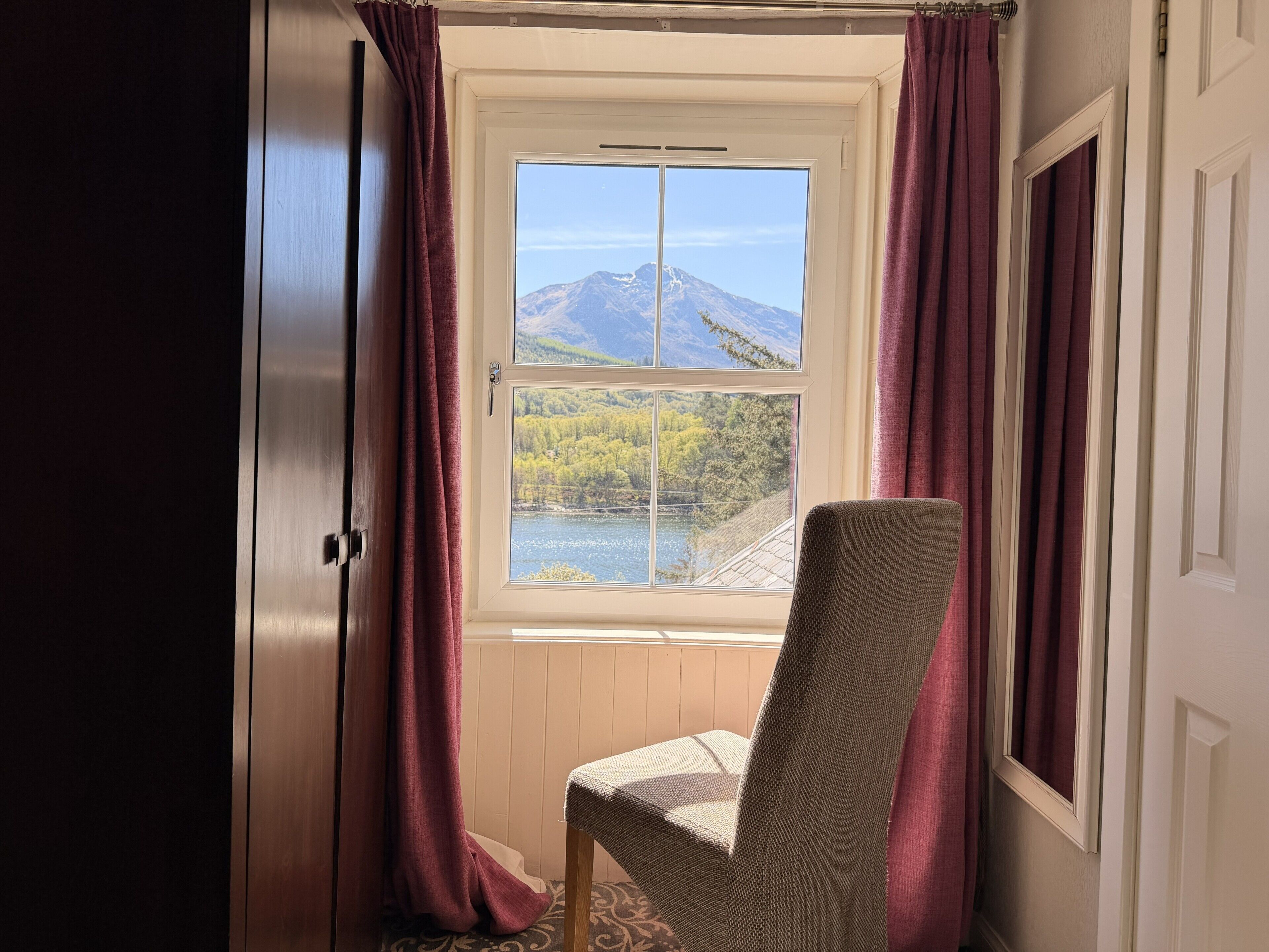 A room with a view of a mountain and a lake through a window, a chair, and a door.