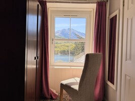 Una habitación con vista a una montaña y un lago a través de una ventana, una silla y una puerta.