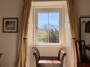 A room with a window overlooking a mountain, a framed picture on the wall, and a wooden bench. - Loch Leven Hotel & Distillery (Fort William)