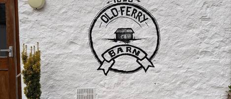 A building with a white exterior wall featuring a black stamp that reads 'OLD FERRY BARNS 1650'.