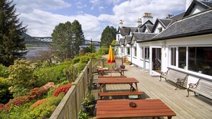 A wooden deck with picnic tables and benches, overlooking a river and a bridge. - Loch Leven Hotel & Distillery (Fort William)