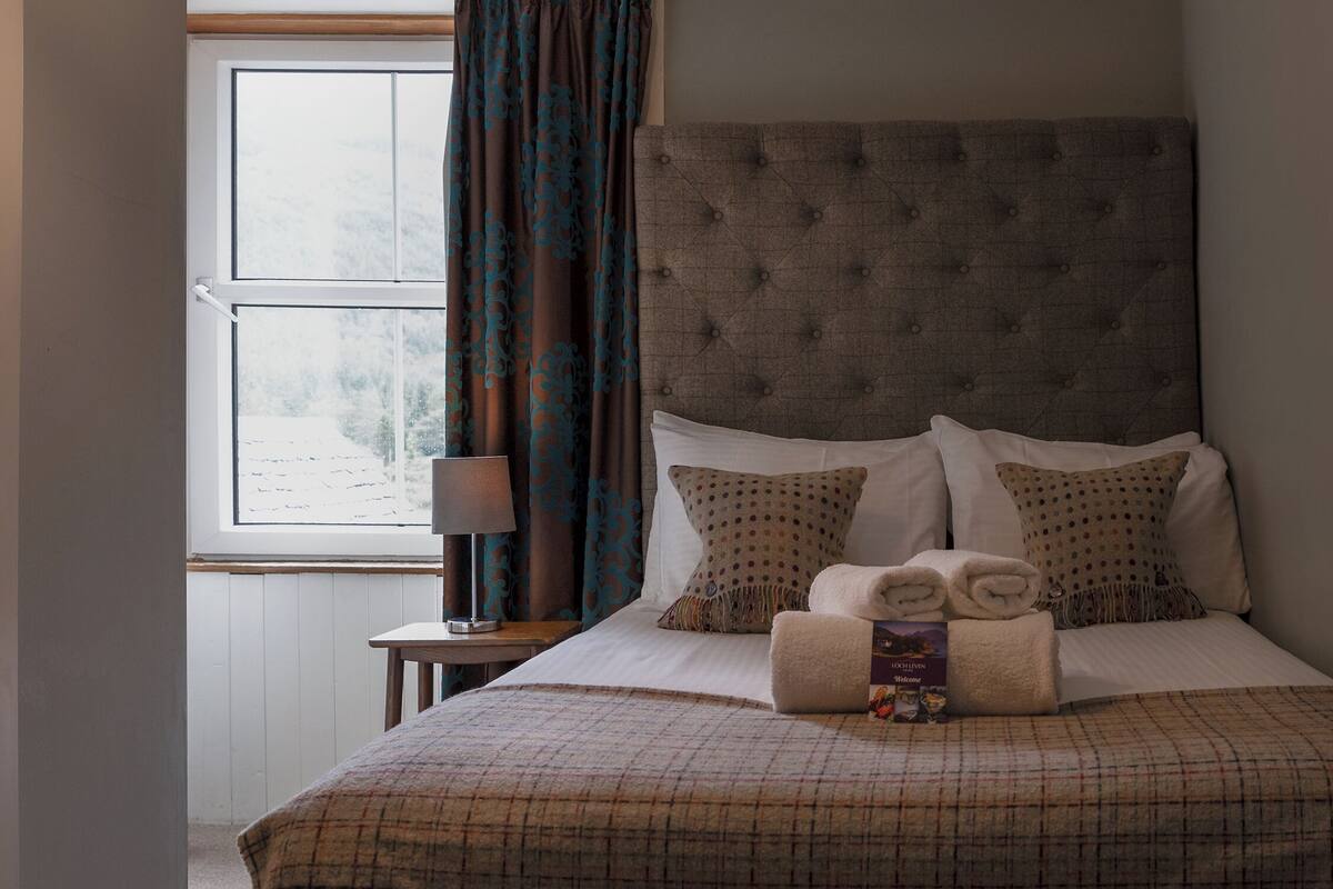 A neatly made bed with a plaid bedspread, two pillows with polka dots, and a folded towel on the bed.