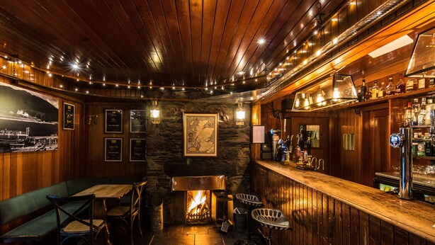 Un rincón de bar acogedor con paredes de madera, una chimenea y una barra con diferentes botellas.