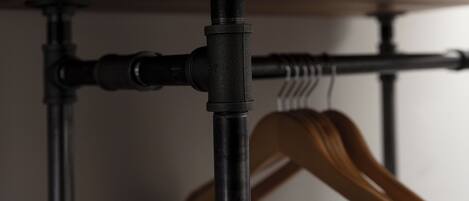 A close-up of a metal pipe and a wooden hanger rod under a shelf.