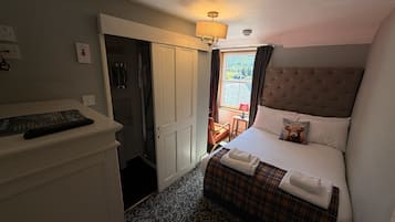 Habitación de hotel con cama, mesita de noche, lámpara, zona de ducha y vistas al exterior.