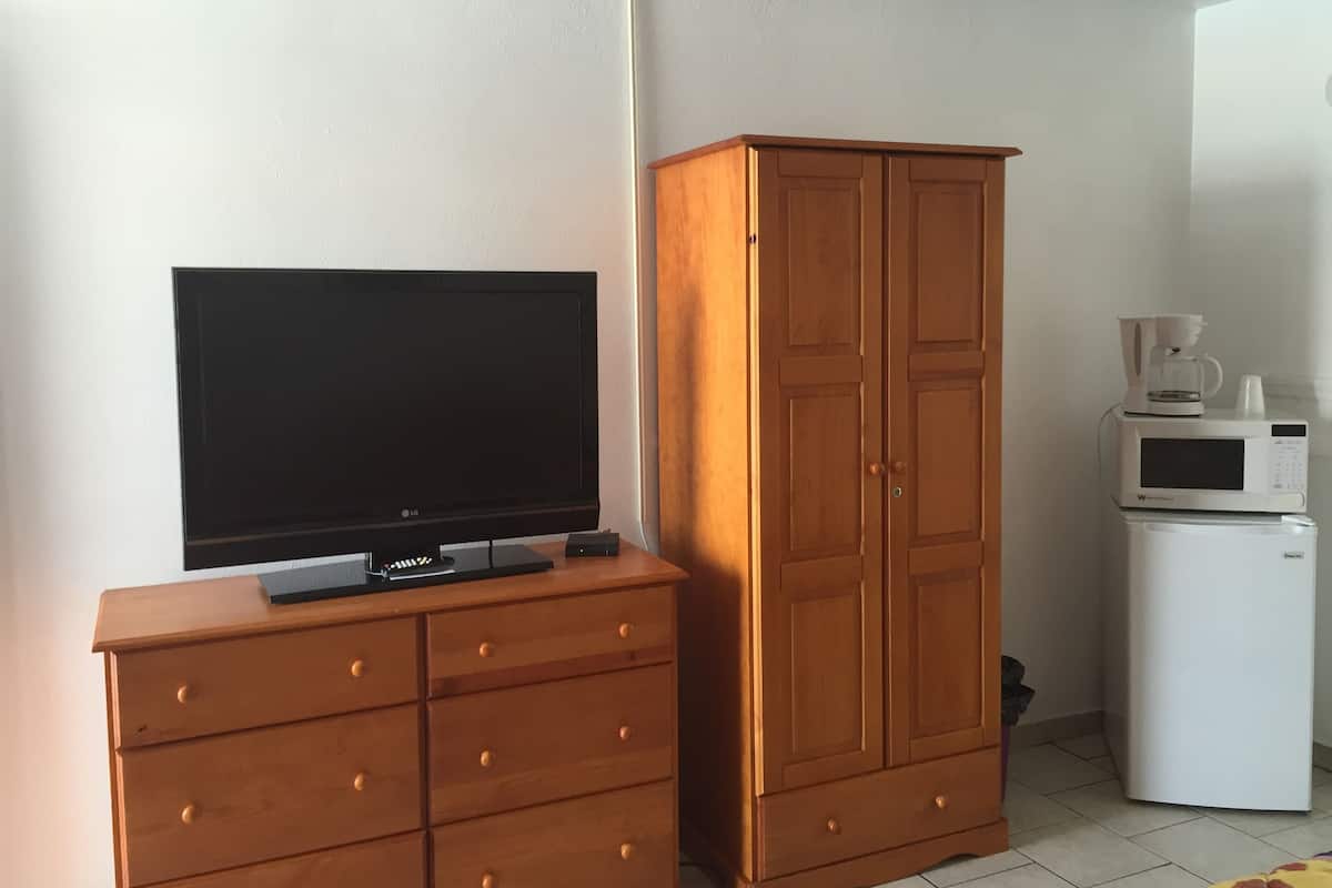 A room with a TV on a wooden dresser, a wardrobe, and a microwave.