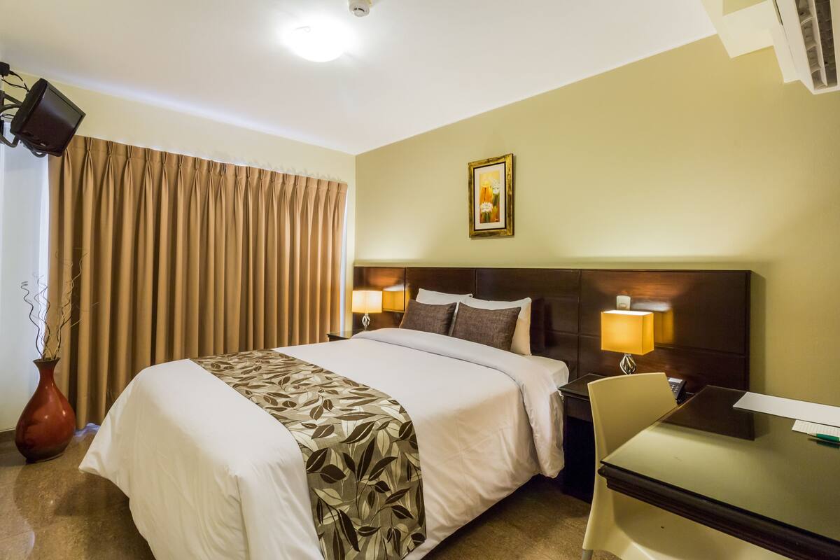 A hotel room with a large bed, two bedside lamps, a desk, and a chair.