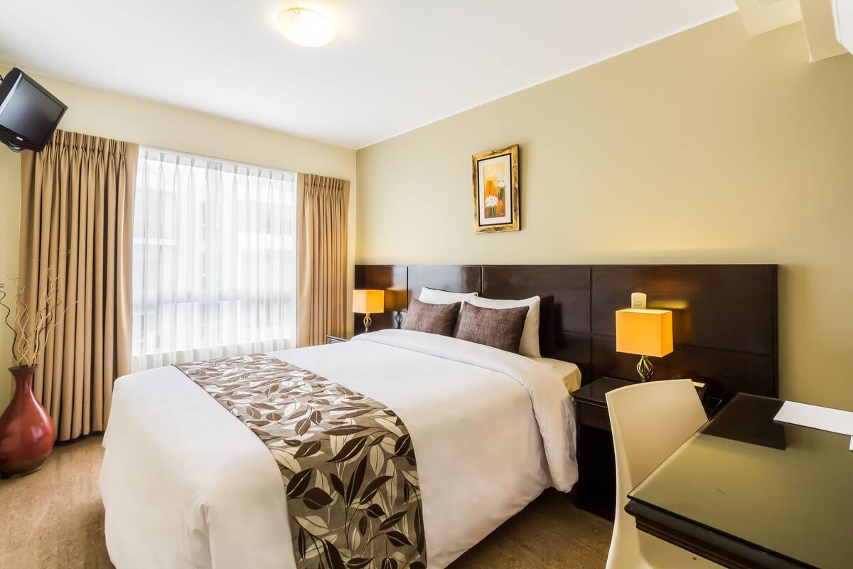 A hotel room with a large bed, two bedside lamps, a desk, and a chair.