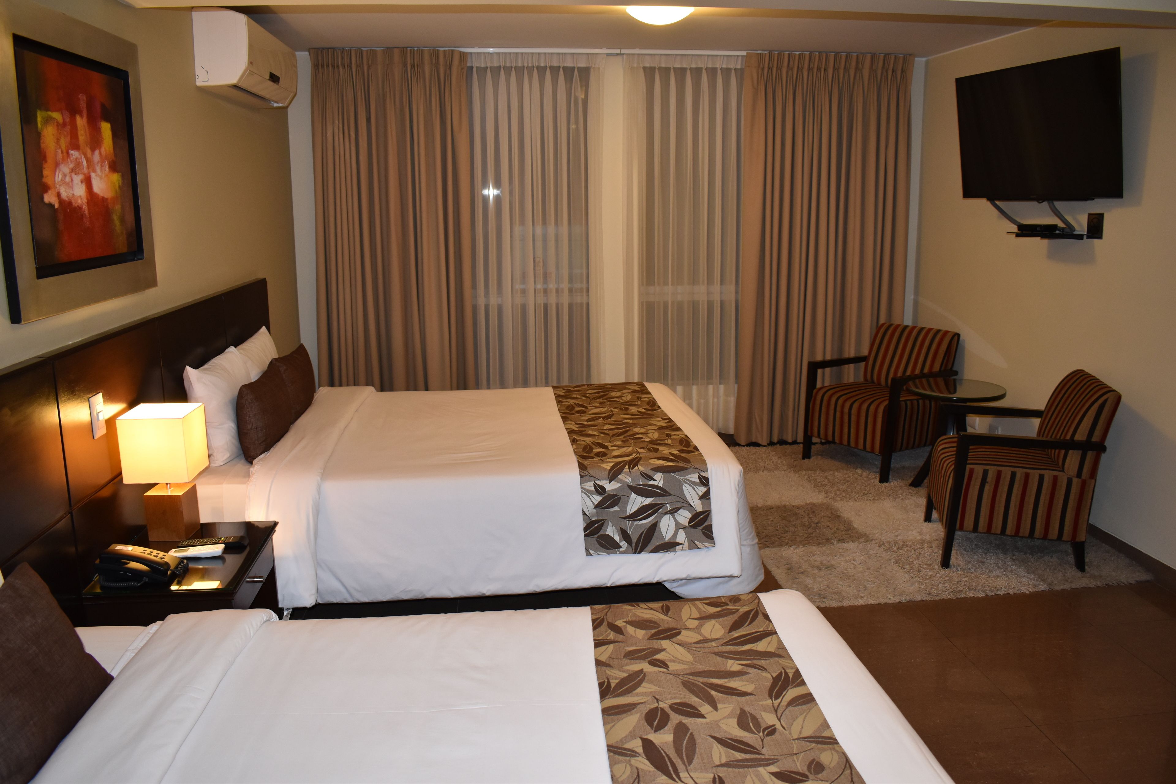 A hotel room with two beds, a TV, a desk with a chair, and a window with curtains.