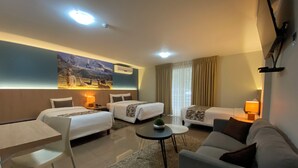 A hotel room with two single beds, a sofa, a small table, and a chair. There is a painting on the wall and an air conditioning unit above the beds. - Hotel El Tambo 1 (Lima)