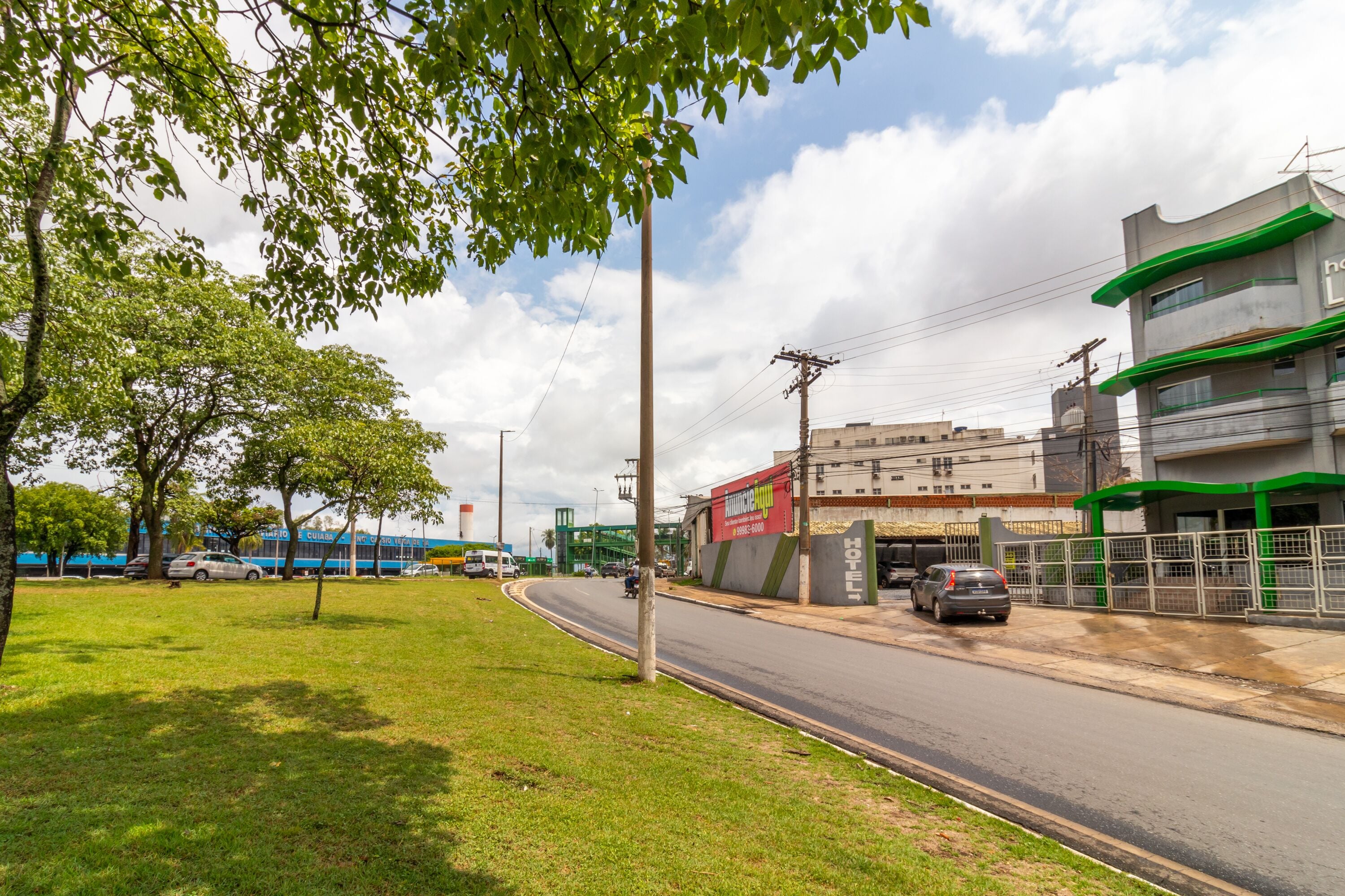 Um hotel com fachada verde e branca, um estacionamento e uma área ajardinada com árvores.