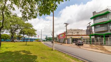 Um hotel com fachada verde e branca, um estacionamento e uma área ajardinada com árvores.