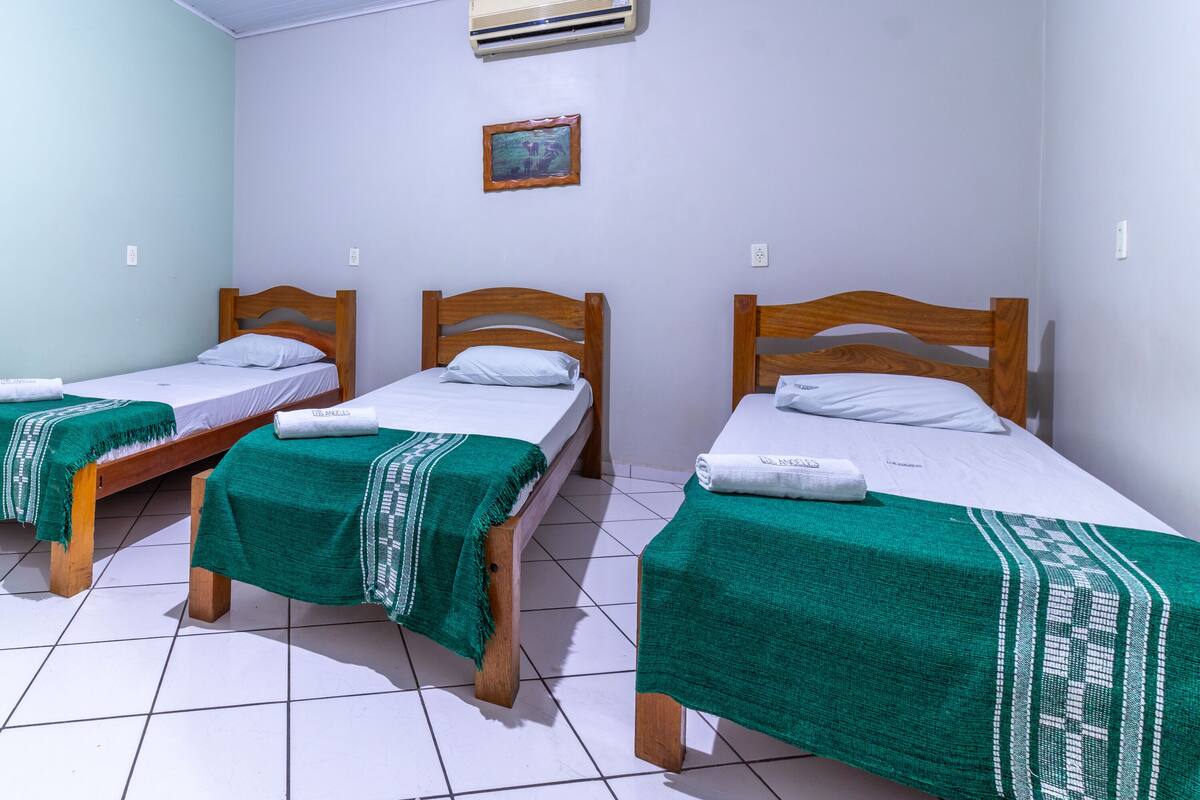 A room with three wooden beds, each with a green blanket and white linens.