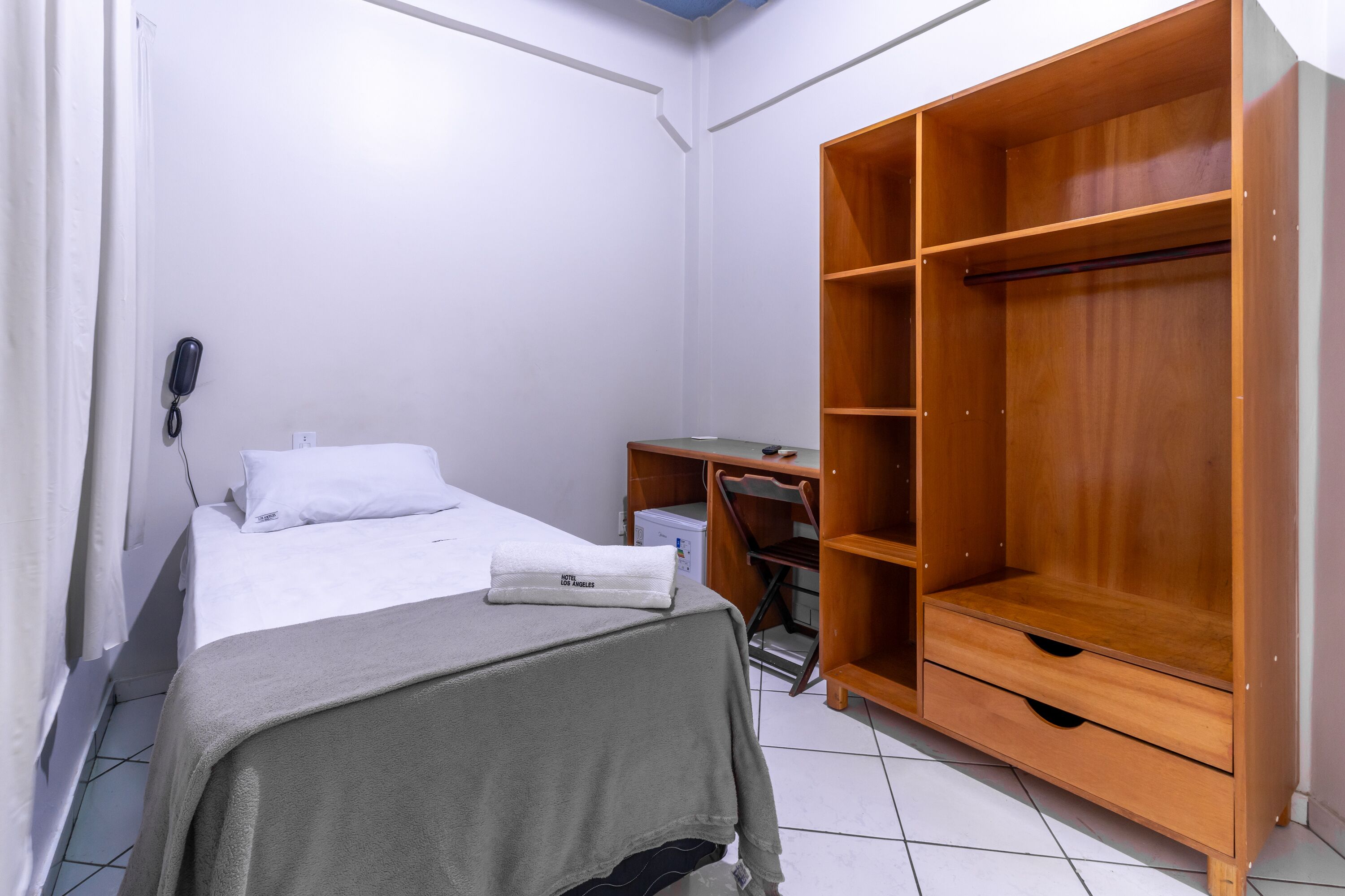 A small, clean room with a bed, a wooden wardrobe, and a desk.