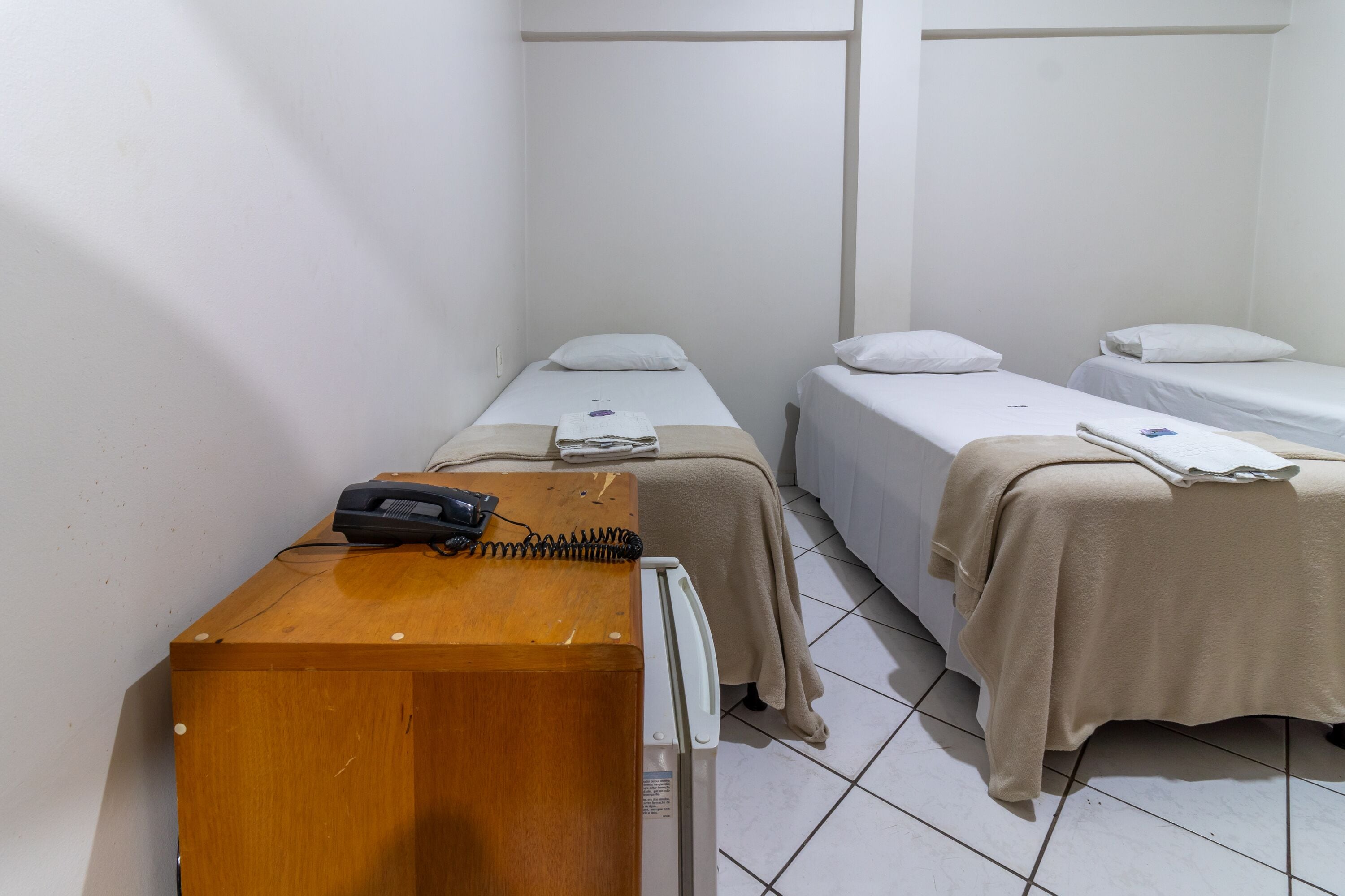 A small, clean room with two single beds, a wooden desk with a telephone and a small heater, and a white radiator.