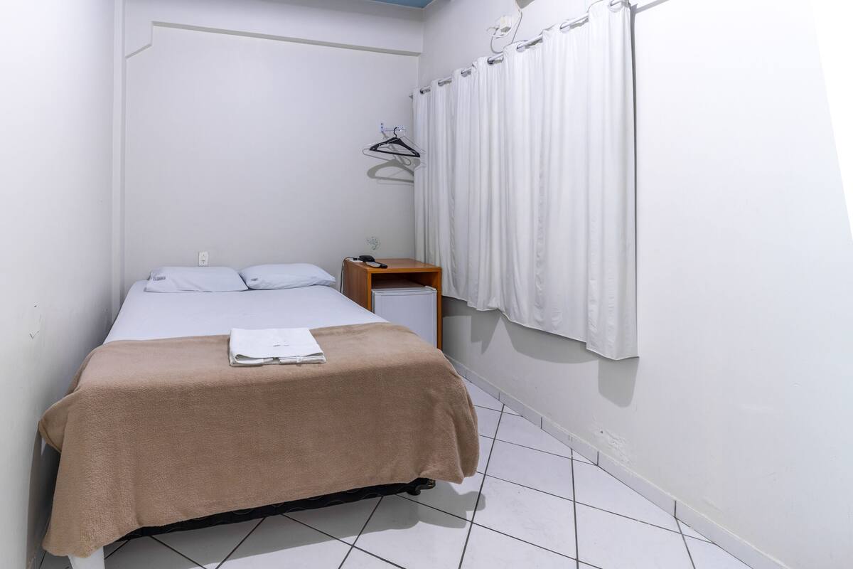 A small, clean room with a single bed, a bedside table, and a wall-mounted heater.