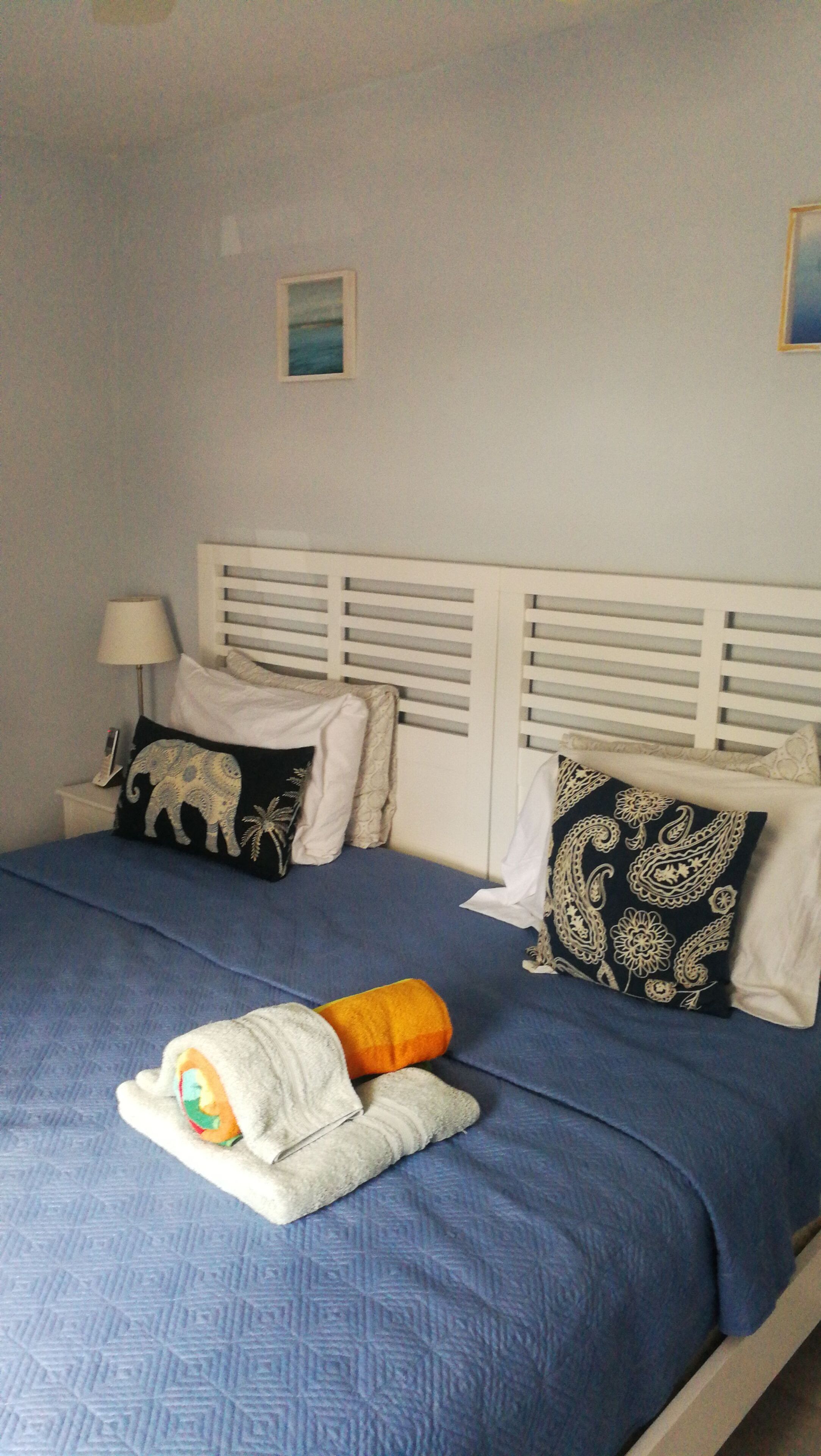 A bed with a blue bedspread, two pillows, a blanket, and a bedside lamp.