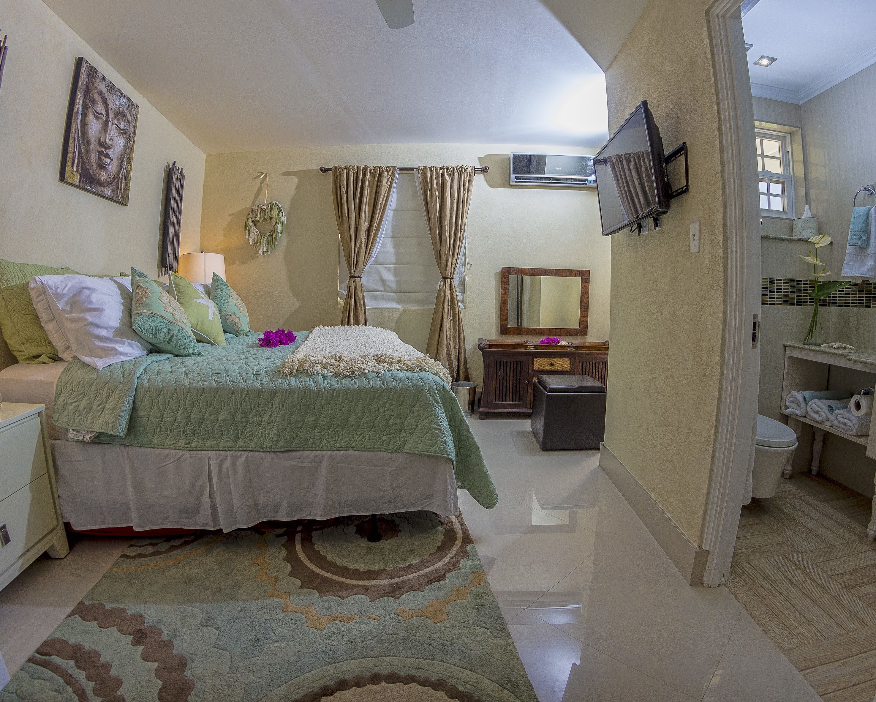 Une chambre à coucher comprenant un lit, une table de chevet, une lampe, des rideaux et un téléviseur fixé au mur.