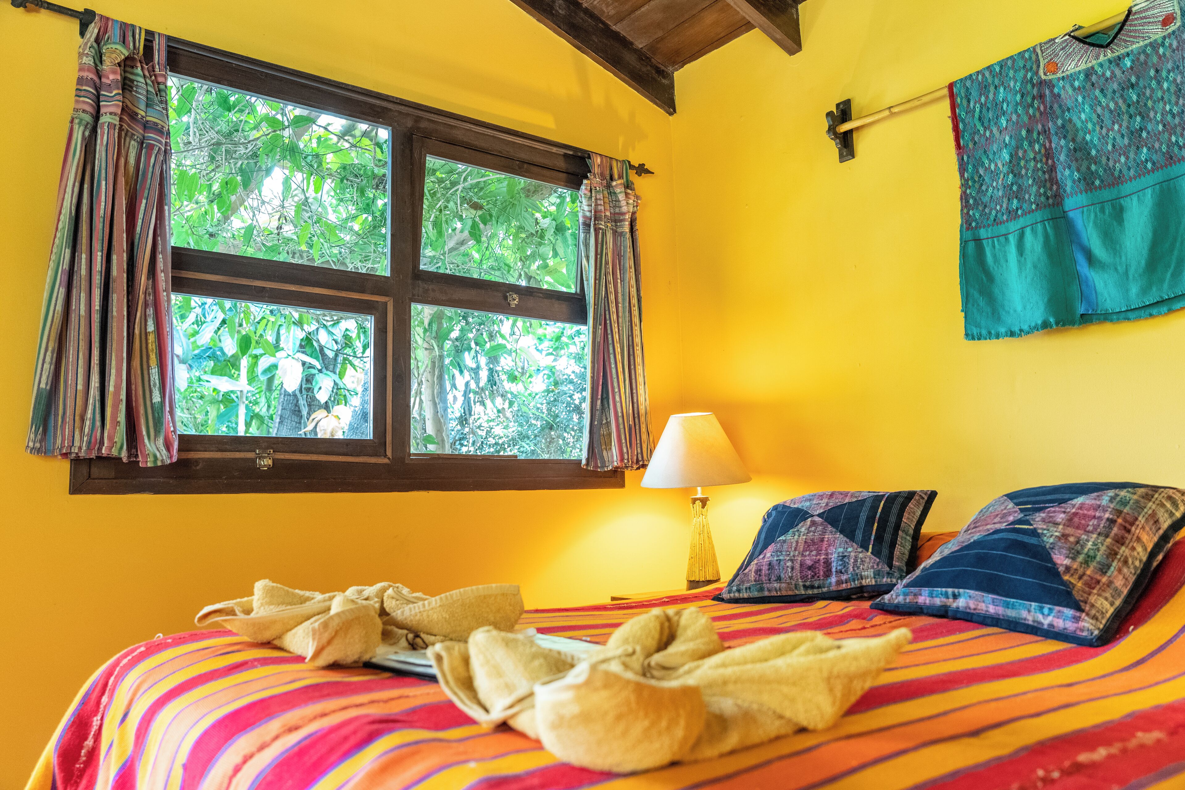A room with a bed, a window with curtains, a lamp, and a wall hanging.