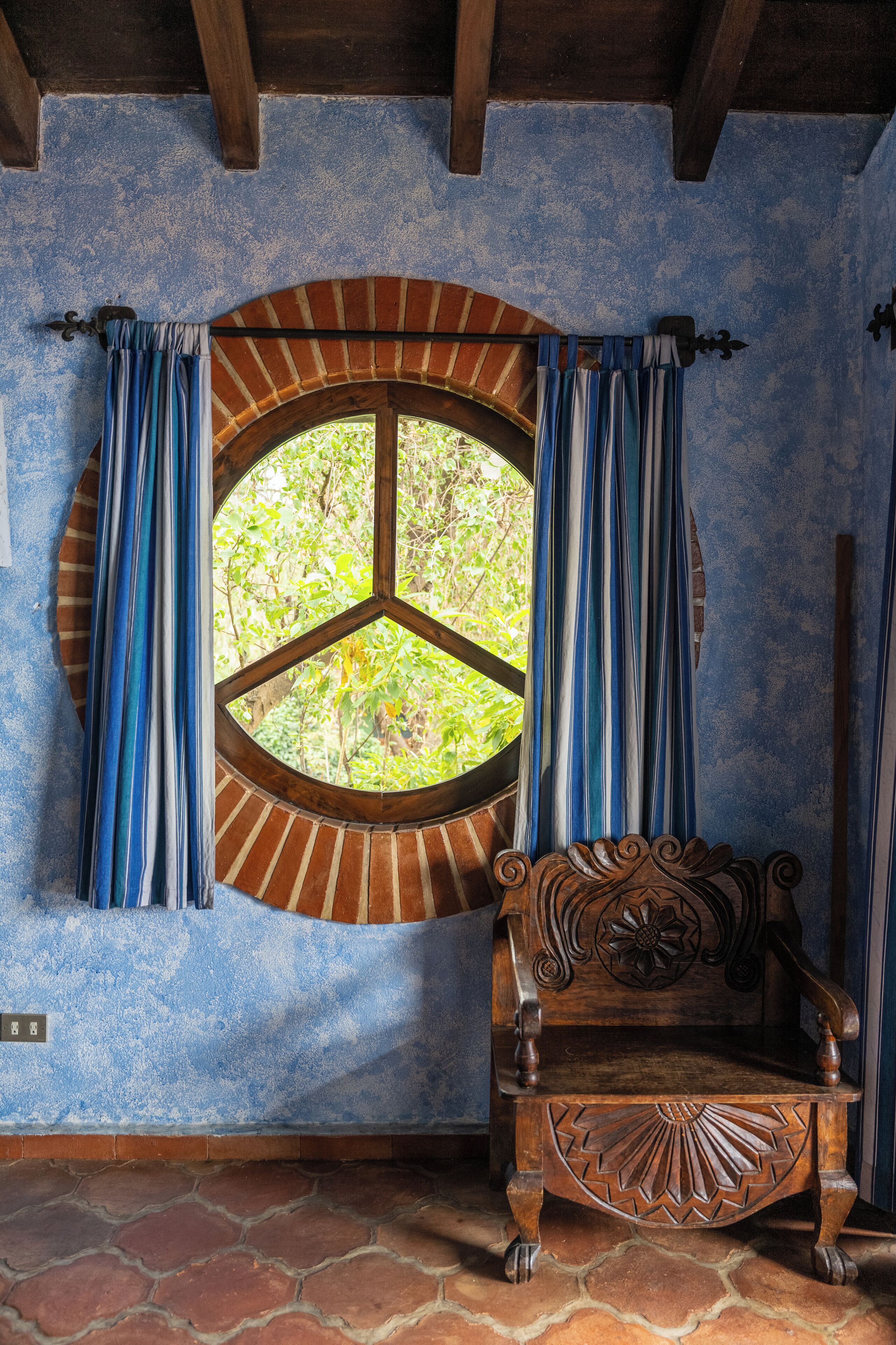 Una habitación con un banco de madera, un ventanal redondo con arco de ladrillo y cortinas azules.