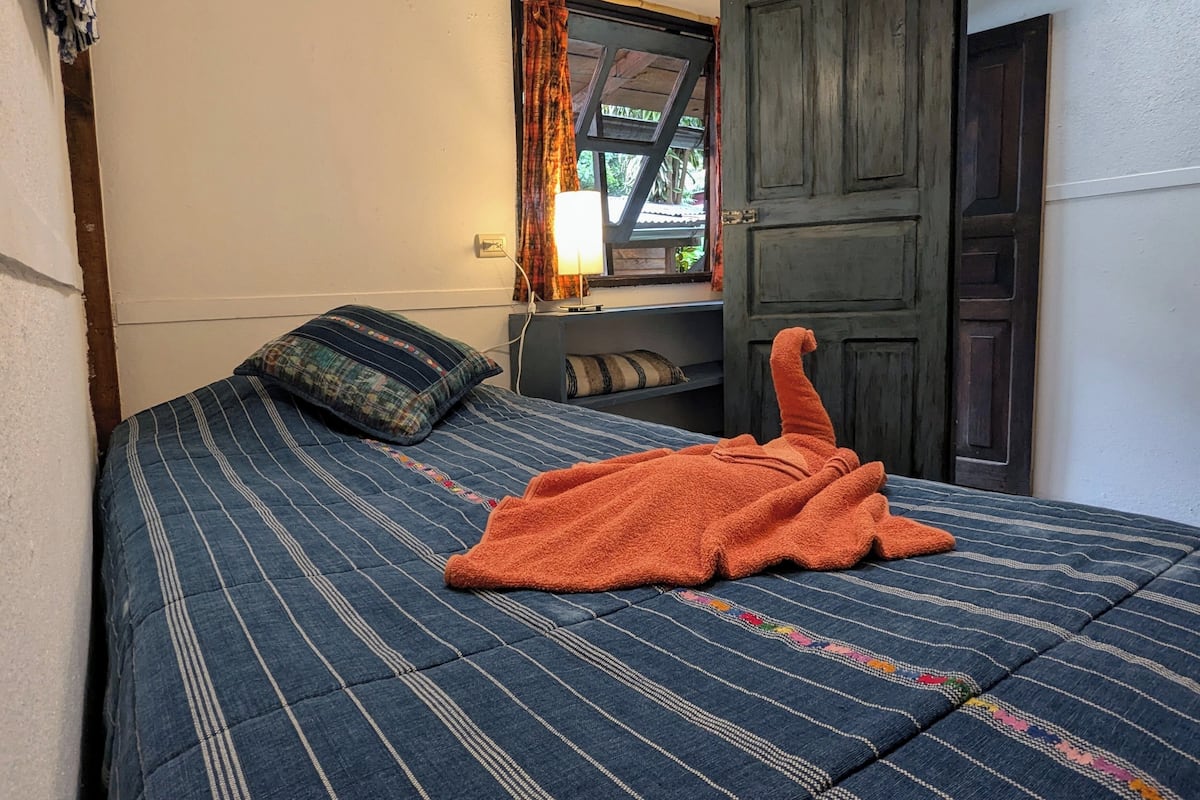 Ein Zimmer mit Bett, einem fensterbepflegten Fenster, einer Tür und einem kleinen Tisch mit Lampe.