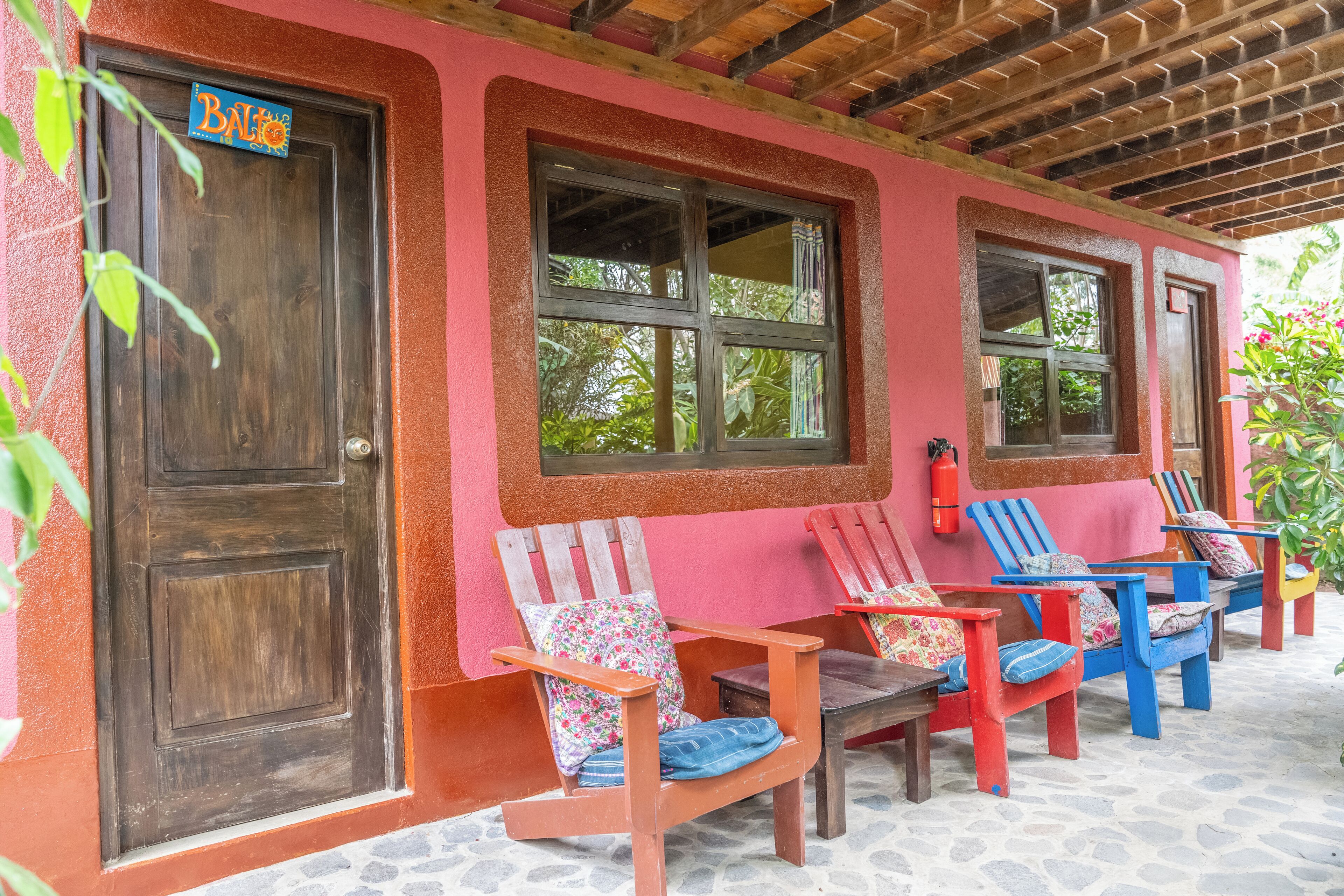 Un bâtiment avec une porte et des fenêtres en bois, des chaises colorées et un extincteur.