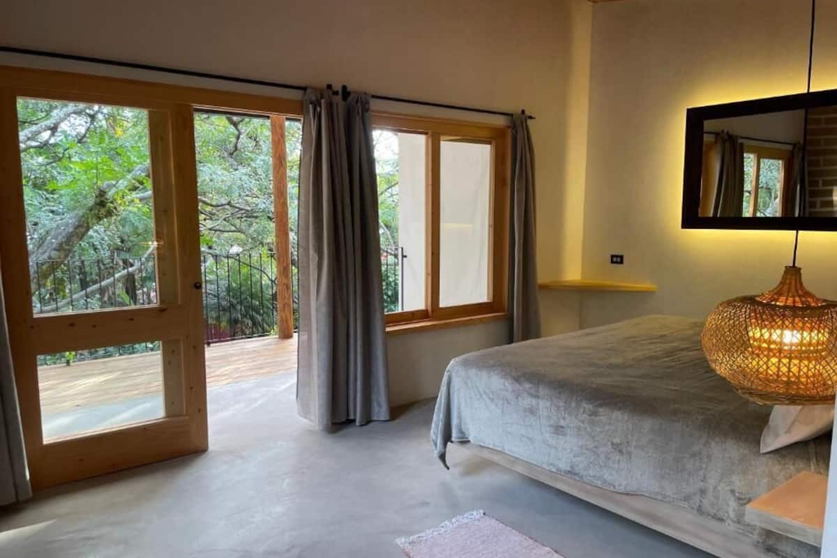 Ein Schlafzimmer mit einem großen Bett, einem Fenster mit Vorhängen, einem Spiegel und einer Hängelampe.