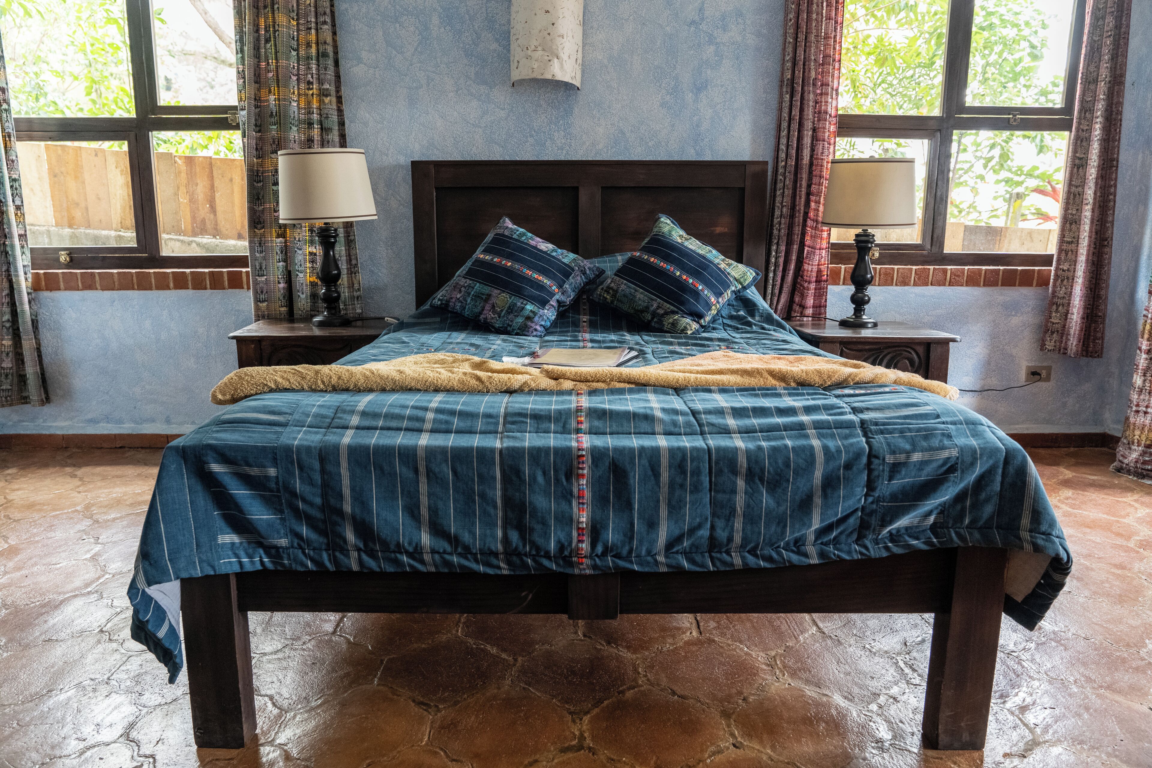 A bedroom with a large bed, two bedside tables, a window with curtains, and a lamp on each table.