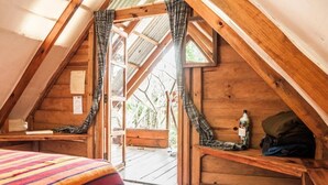 Ein gemütliches Schlafzimmer im Dachgeschoss mit schrägen Wänden, Holzboden und einem Fenster mit Vorhängen.