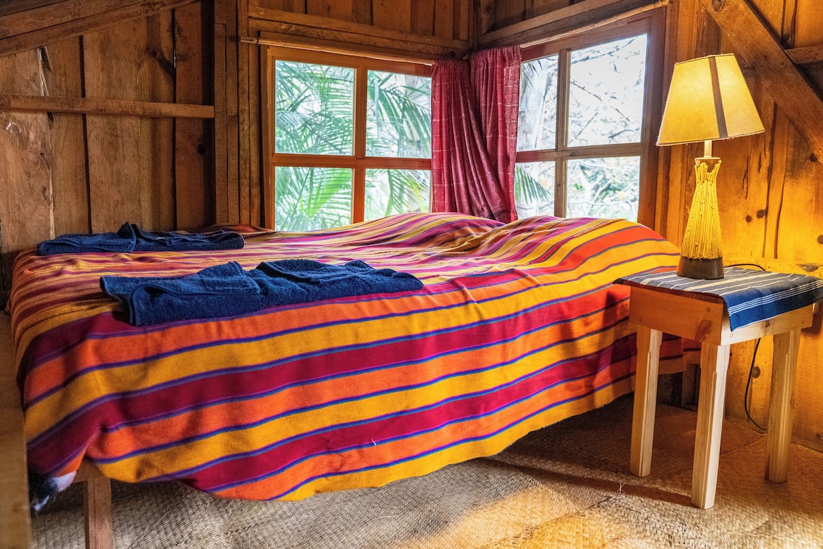 Ein Zimmer in einer Holzhütte mit einem Bett, einem kleinen Tisch und einem Fenster mit Vorhängen.