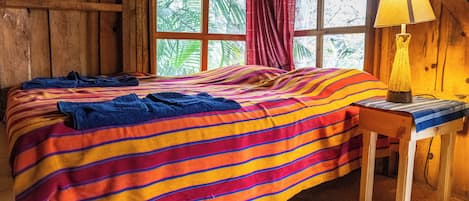 Ein Zimmer in einer Holzhütte mit einem Bett, einem kleinen Tisch und einem Fenster mit Vorhängen.