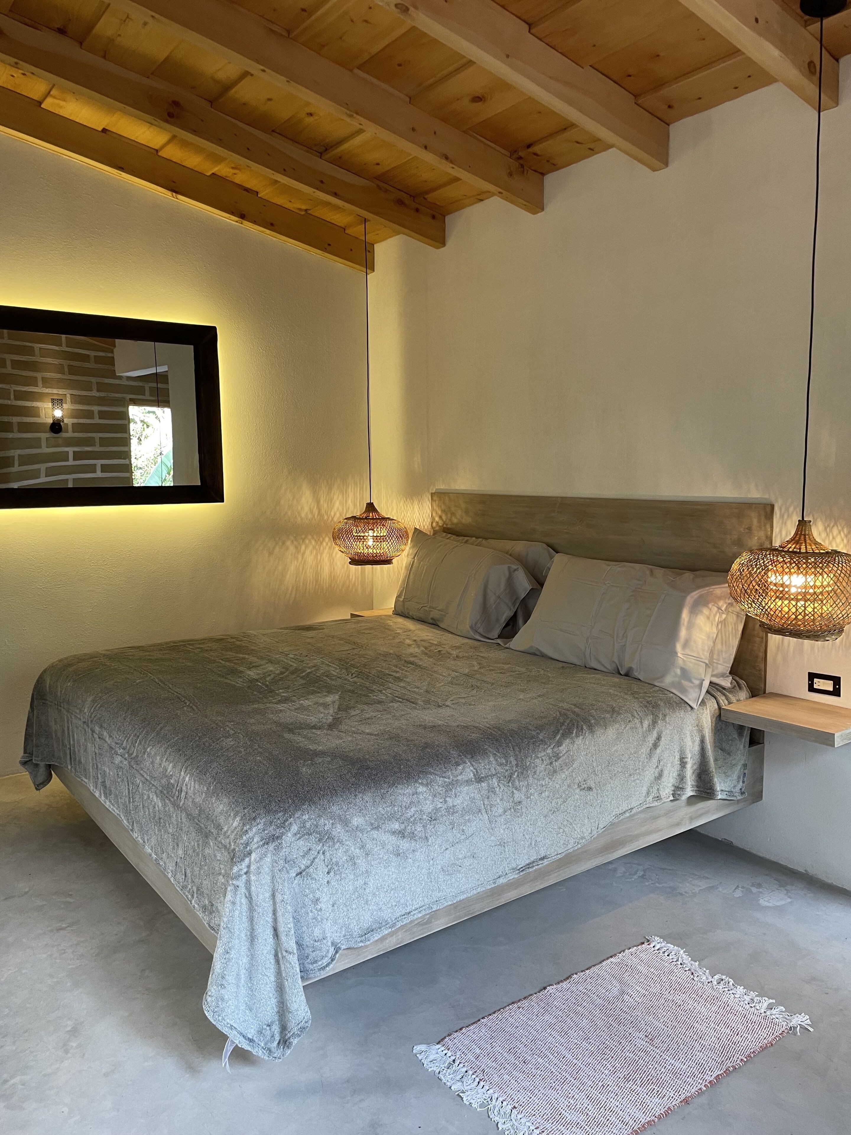 Ein Schlafzimmer mit einem Bett, Holzbalken, einer Hängeleuchte und einer Wandleuchte.