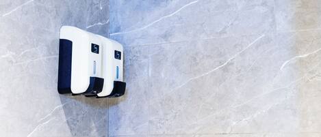 A bathroom with a shower, a hand soap dispenser, and a faucet.