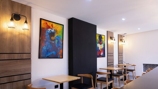 Een modern interieur met houten paneelwanden, abstracte schilderijen en eenvoudige houten tafels en stoelen.