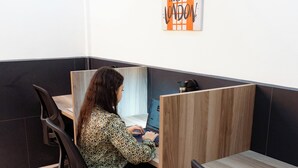 Een werkplek met een persoon zittend aan een bureau, een poster aan de muur en een scheiding tussen werkplekken.