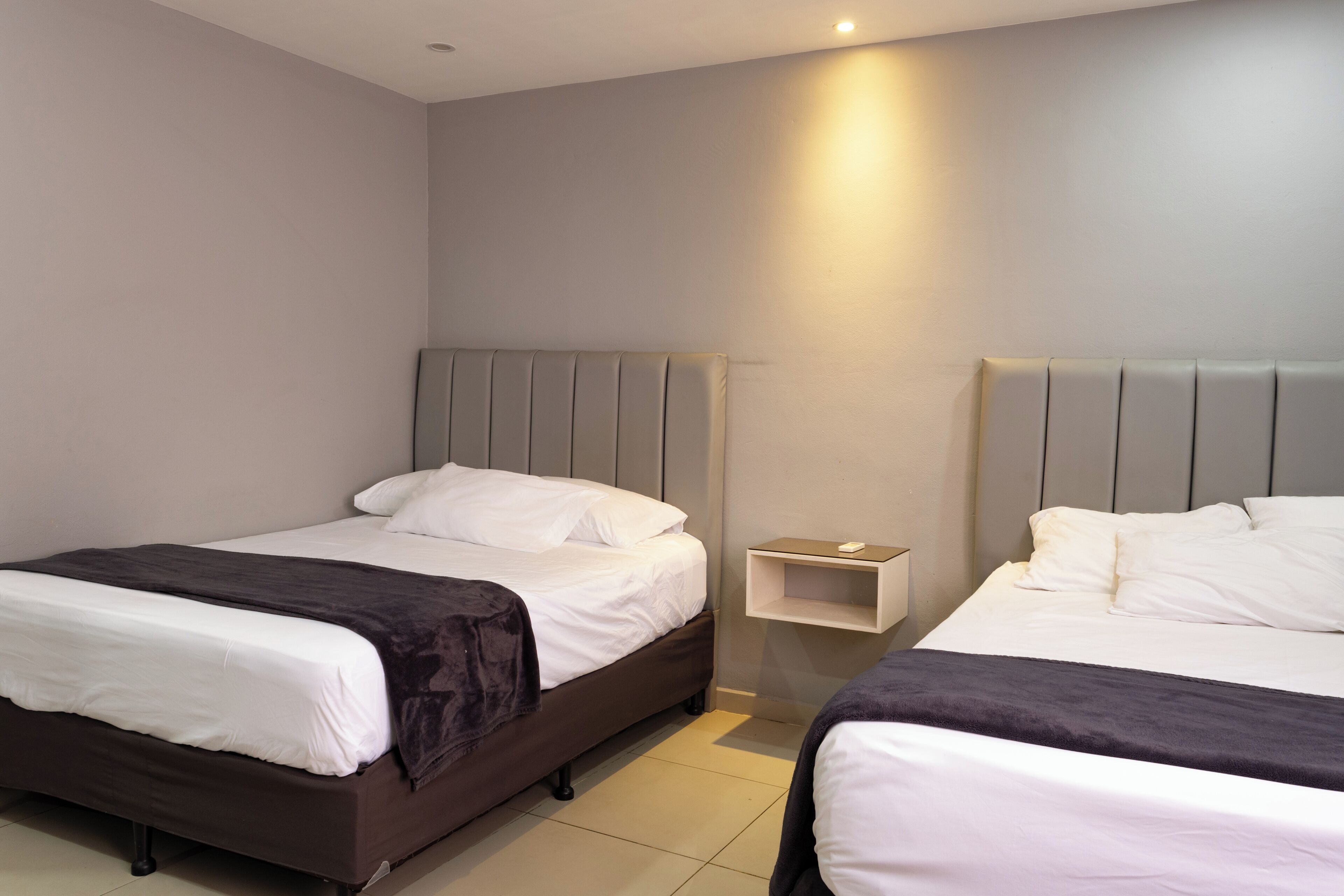 Ein Hotelzimmer mit zwei Betten, einem Nachttisch und einem an der Wand befestigten Regal.