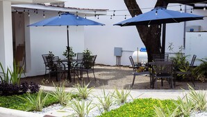Een terras met tafels en stoelen, omringd door planten en een grindpad.