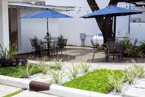 An outdoor seating area with tables and chairs, surrounded by plants and a gravel path. - Micro Hotel Rio de Piedras (San Pedro Sula)