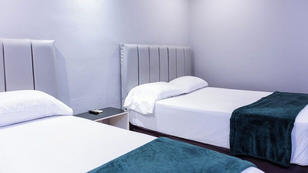 Quarto de hotel com duas camas, uma mesa de cabeceira e painel de cabeceira fixado na parede.