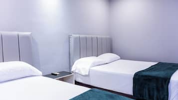 Habitación de hotel con dos camas, una mesita de noche y un cabecero fijado a la pared.