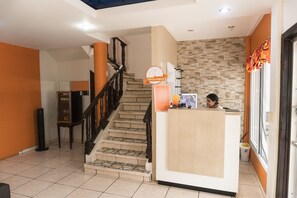 Check-in at the reception desk, surrounded by a mix of patterned and plain tiles and a staircase with a handrail.