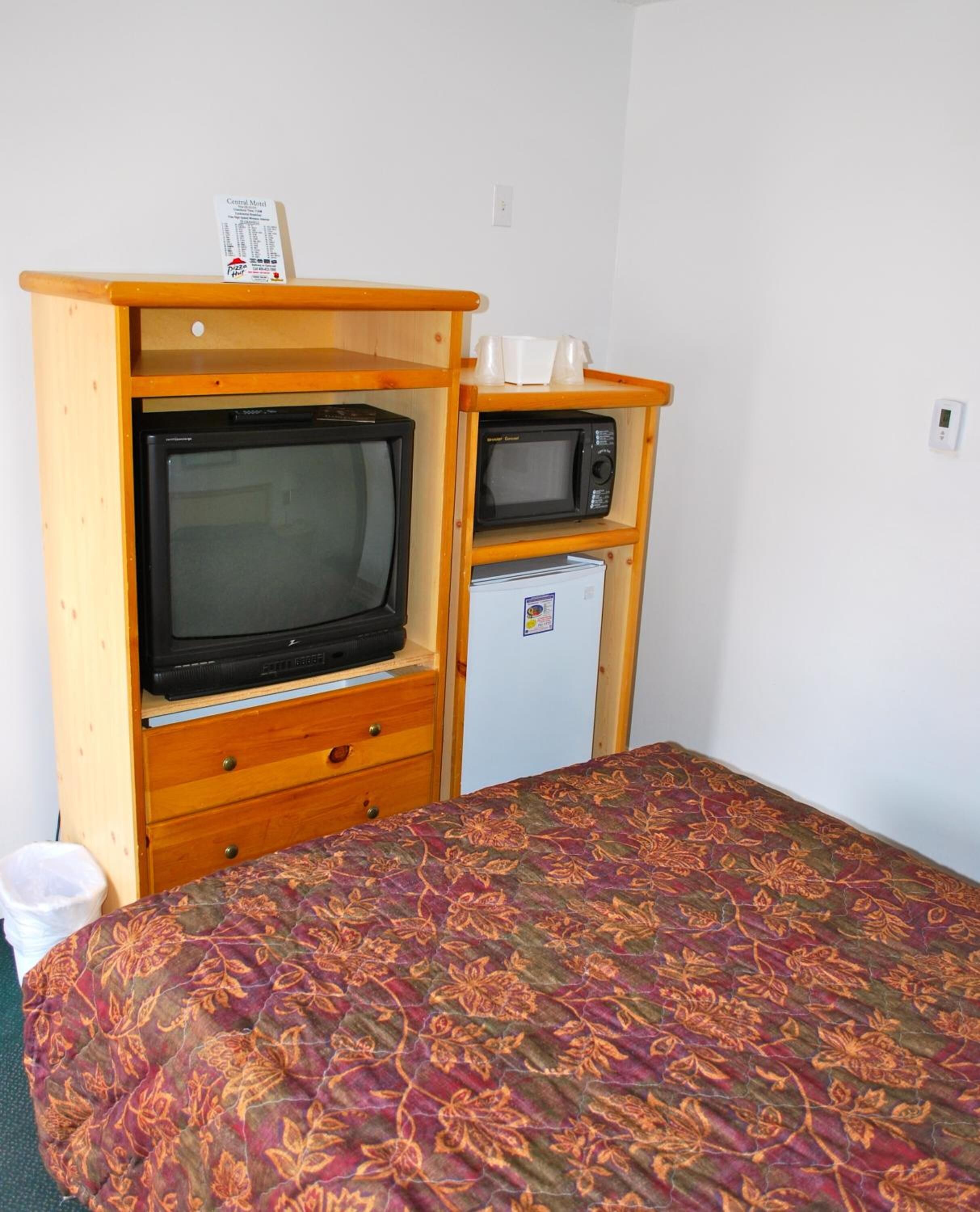Une pièce de taille modeste comprenant un lit, une armoire en bois avec une télévision et un four à micro-ondes, ainsi qu’un petit réfrigérateur.