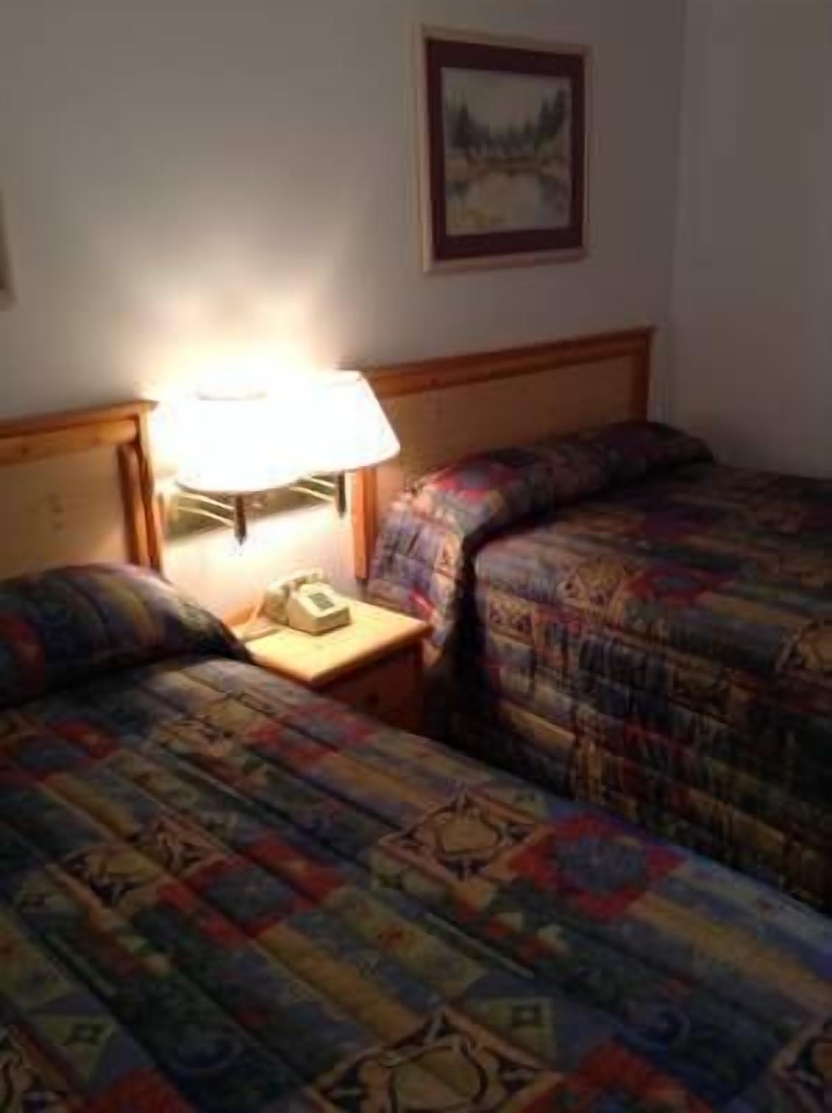 A hotel room with two beds, a nightstand with a lamp, and a framed picture on the wall.